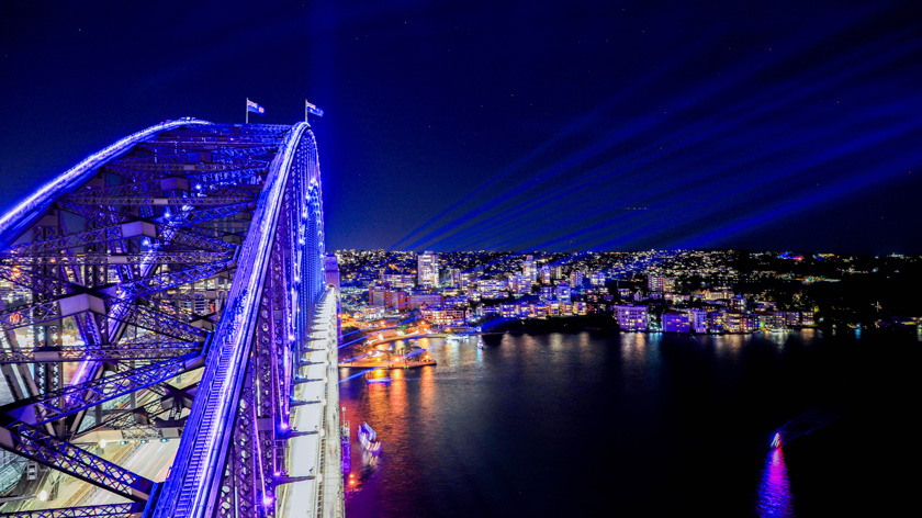 view of the sydney harbour bridge lit up blue and purple for the vivid sydney festival as seen from the top of the pylon lookout